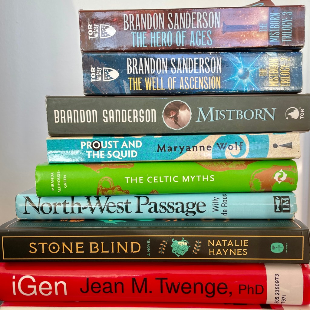 A stack of books. From bottom to top: iGen, Jean M. Twenge; Stone Blind, Natalie Haynes; North-West Passage, Willy de Roos; The Celtic Myths, Miranda Aldhouse-Green; Proust and the Squid, Maryanne Wolf; Mistborn Trilogy, Brandon Sanderson.