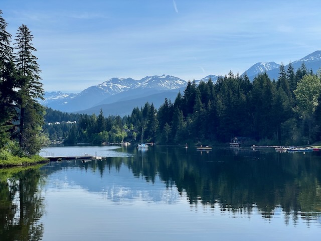A lake surrounded by forest, with snowcapped mountains in the background.